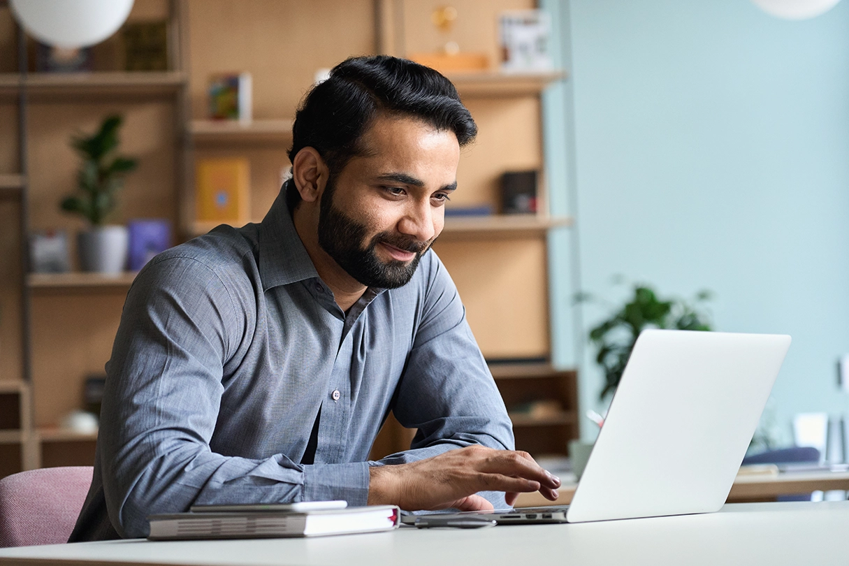 Smiling indian business man working on laptop at home office