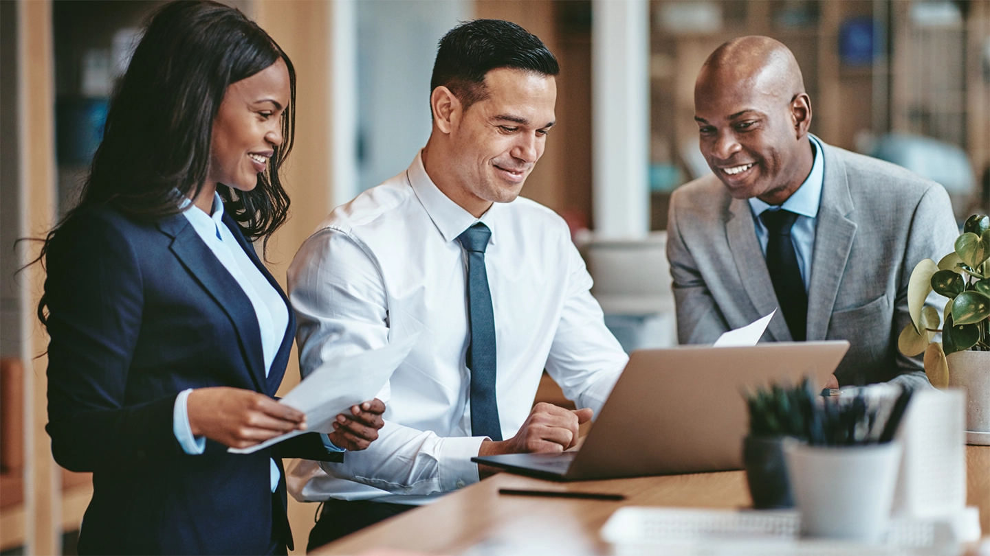 trio of business people happily gathered around a laptop