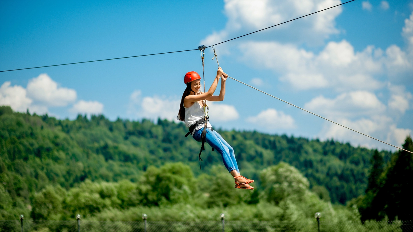 woman on a zip line in the the forest bright blue sky