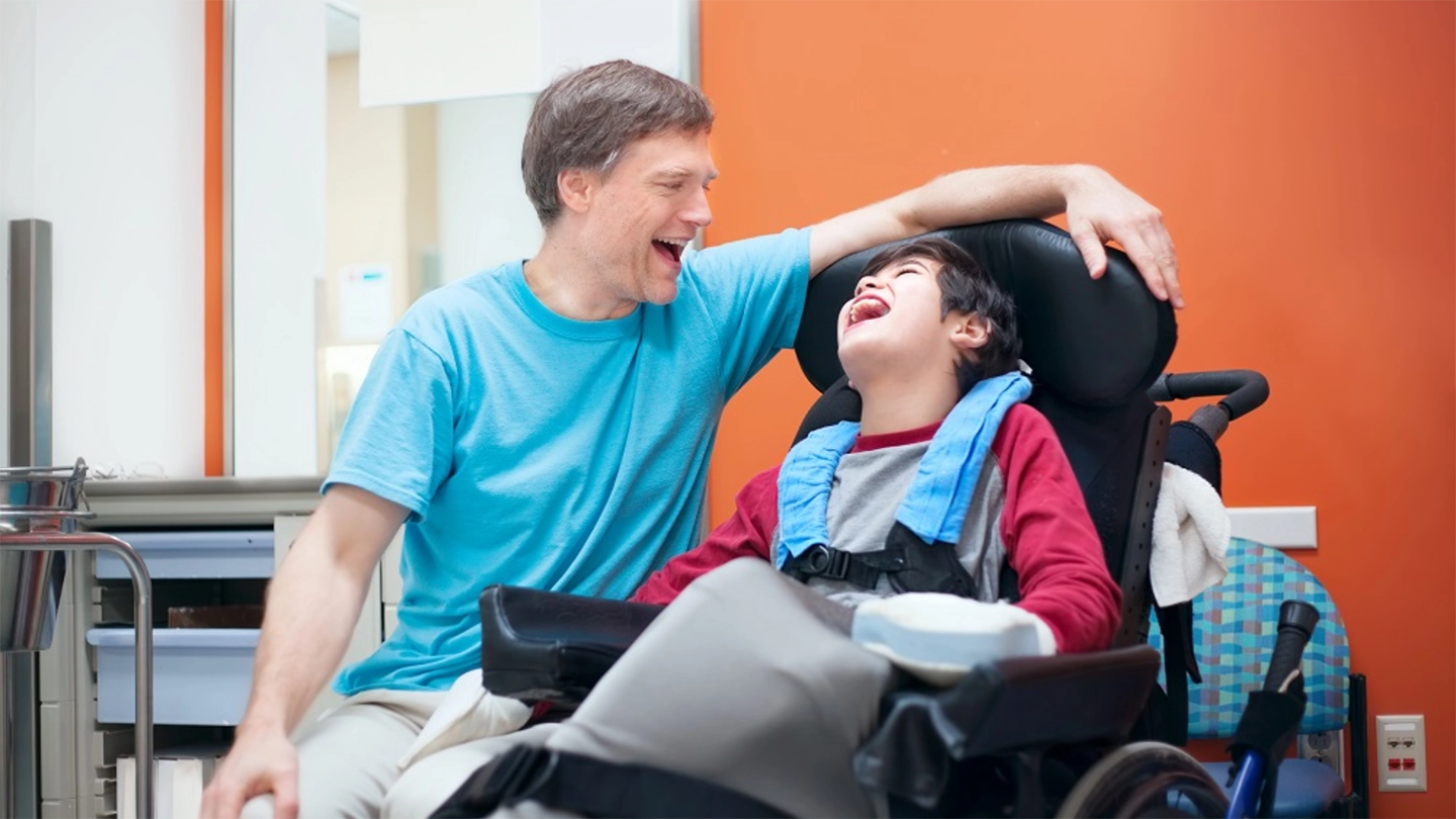 social worker laughs with young boy in wheelchair